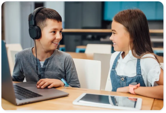 Un garçon et une fille devant ordinateur portable et tablette.